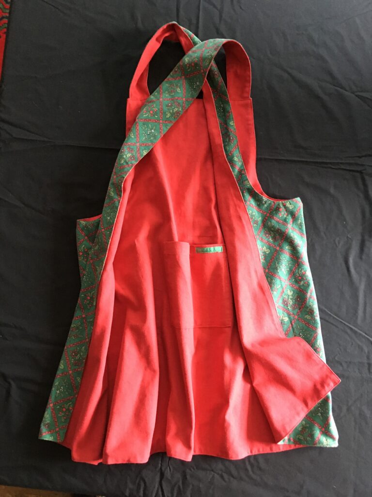 Pinny 180 showing both festive patterned side and plain scarlet red side