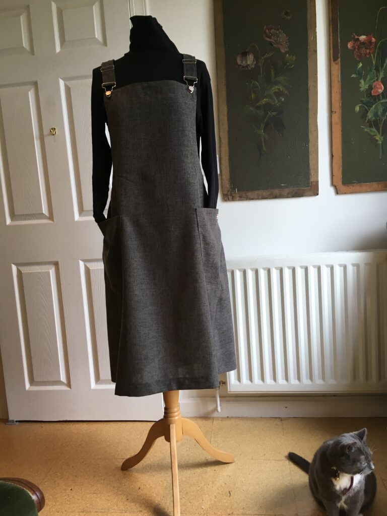 Charcoal polyester pinafore dress on mannequin, with cat photo-bombing foreground.